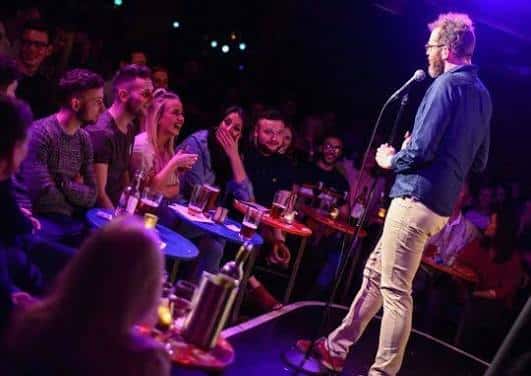Comediante actuando en el escenario frente a una audiencia en mesas