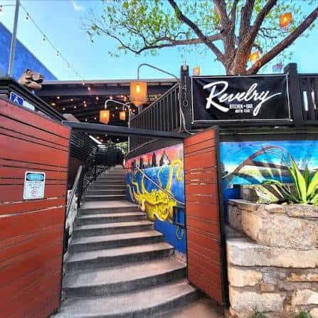 Escalera de entrada con murales coloridos y letrero de Revelry Kitchen + Bar