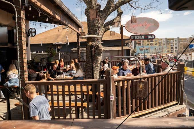 Terraza exterior del restaurante con mesas de picnic bajo árboles y ambiente diurno