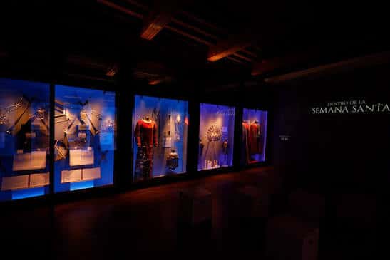Interior del museo con vitrinas iluminadas en azul mostrando vestimenta religiosa y objetos de Semana Santa