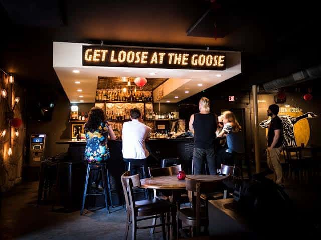Vista general del interior con letrero 'GET LOOSE AT THE GOOSE' y clientes en la barra