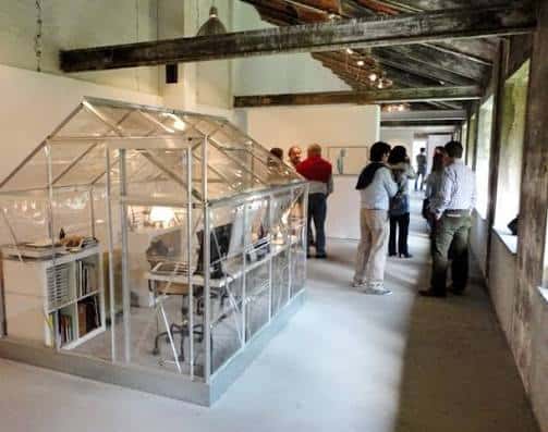 Vista interior de la galería durante una exposición con visitantes y estructura de cristal