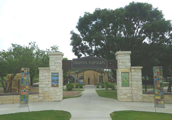 Entrada principal al parque con letrero 'Creative Playscape' y columnas de piedra