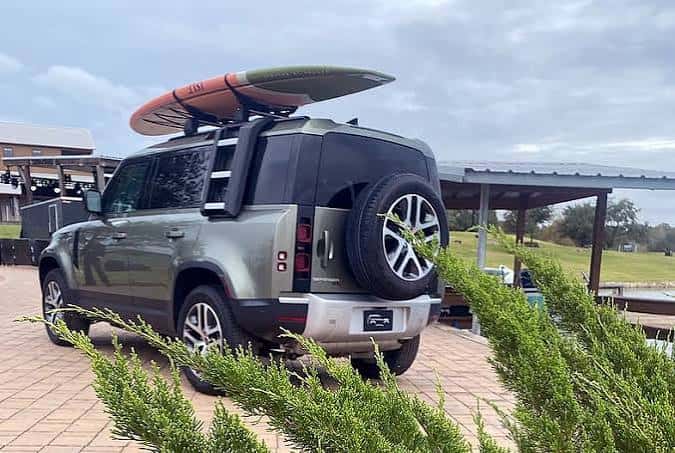 Land Rover Defender verde con tabla de surf en el techo
