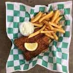 Porción de pescado empanizado con limón y salsa blanca sobre papel cuadriculado