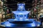 Fuente iluminada en azul durante la noche con luces decorativas colgantes