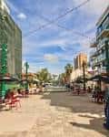 Plaza al aire libre con mesas de restaurante, sombrillas verdes y cielo despejado