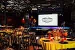 Interior del salón de eventos con mesas redondas y pantalla de proyección