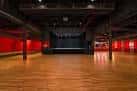Espacio vacío del salón principal con escenario y piso de madera, ideal para eventos