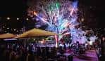 Vista nocturna del Axelrad Beer Garden con árboles iluminados y mesas al aire libre