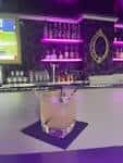 Vista cercana de la barra con botellas iluminadas y una bebida en primer plano