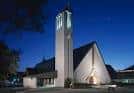 Fachada nocturna de la iglesia iluminada con torre y techo triangular