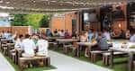 Terraza al aire libre con mesas largas y personas disfrutando en un ambiente festivo
