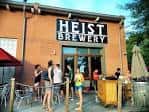 Entrada exterior de Heist Brewery con clientes en la terraza bajo el sol