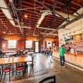 Interior del bar de Triple C Brewing Company con techo industrial y mesas de madera