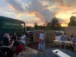 Terraza exterior al atardecer con mesas y personas socializando en Town Brewing Co