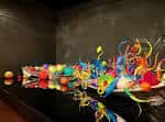 Exposición de pequeñas obras de arte en vidrio multicolor sobre superficie reflectante