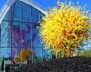 Detalle exterior con árbol de vidrio amarillo frente a la estructura de cristal azul