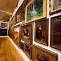 Galería interior del museo con múltiples cuadros enmarcados colgados en pared de madera oscura