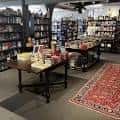 Área interior de la librería con alfombra decorativa y mesas de productos destacados
