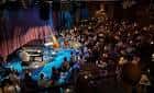 Interior del salón de jazz con escenario iluminado y público sentado en mesas durante un concierto