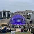 Evento diurno frente al escenario con arquitectura distintiva y audiencia en césped