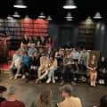 Escenario con actores y público en ambiente íntimo de obra teatral