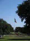 Área verde del parque con la bandera al fondo y árboles frondosos
