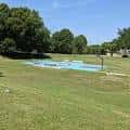 Vista panorámica de Greenville Park con césped verde y estanque bajo cielo azul