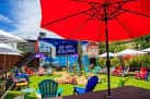Área exterior del Social Beer Garden HTX con mesas, sillas coloridas y sombrillas bajo un cielo despejado