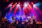 Concierto en vivo en el escenario del Visulite Theatre con iluminación de colores vibrantes