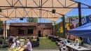 Área diurna del venue con estructura metálica, mesas y zona verde para eventos al aire libre