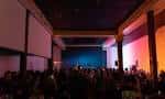 Interior del salón de eventos con escenario iluminado y público asistiendo a un espectáculo