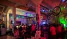 Interior del local durante un evento con iluminación de colores y público asistiendo
