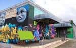 Fachada exterior del Super Happy Fun Land con murales artísticos y esculturas coloridas