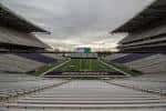 Vista interior del Husky Stadium con gradas vacías y campo de fútbol americano bajo cielo nublado