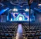 Interior del salón principal de eventos con escenario iluminado, luces de neón y filas de asientos listas para una presentación