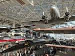 Interior del museo con aeronaves suspendidas y visitantes recorriendo la sala