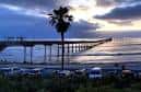 Vista del Ocean Beach Pier al atardecer con palmeras y estacionamiento visible
