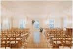Vista frontal de la sala de ceremonias con hileras de sillas de madera y ventanales luminosos