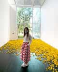 Interior del museo con una instalación artística de flores amarillas en el suelo y una visitante observando