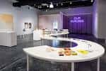 Interior del espacio de exhibición con mesas blancas circulares y arte en las paredes