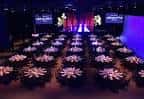 Sala de eventos con mesas redondas decoradas y escenario iluminado
