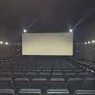 Interior de sala de cine con butacas y pantalla proyectando luz blanca