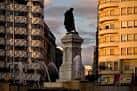 Estatua de Guzmán el Bueno en primer plano con fachadas urbanas al atardecer