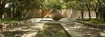 Paisaje arquitectónico con escultura cónica y estanque reflejante entre árboles
