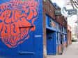 Fachada exterior del Blue Moon Tavern con mural colorido y letrero azul