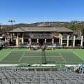 Campo de tenis central con gradas y edificio del club al fondo