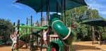 Área de juegos infantiles al aire libre con tobogán verde y sombra en el centro recreativo