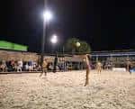 Jugadores de voleibol en cancha de arena durante la noche con iluminación artificial